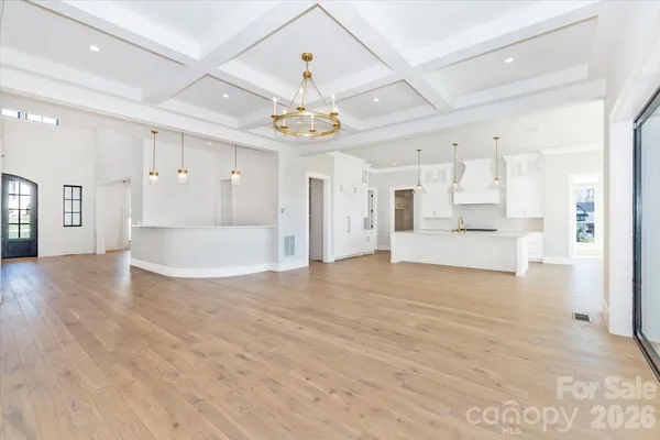a view of an empty room with wooden floor and a kitchen