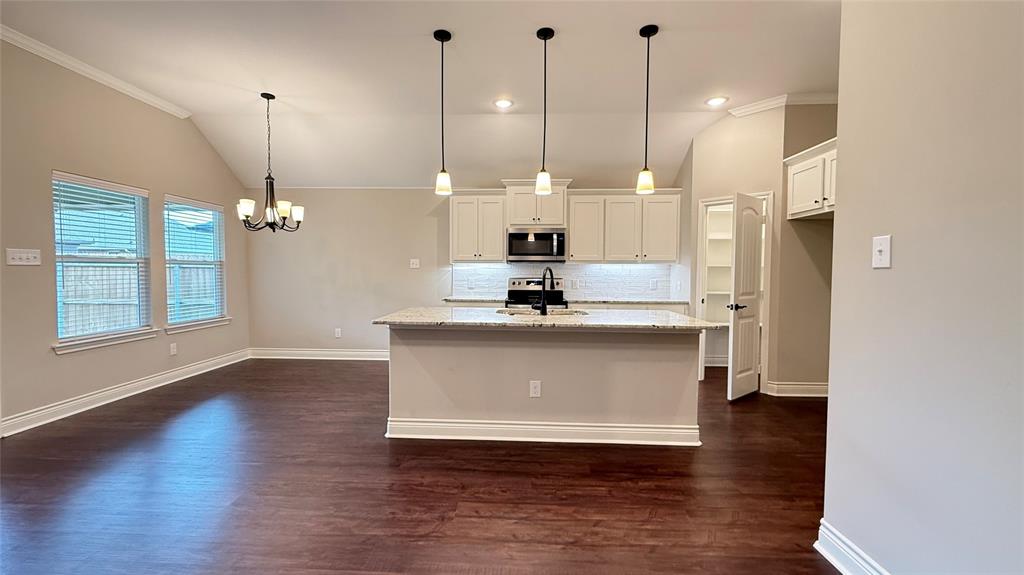 704 Ransom Way Greenville, TX 75402 - Photo 4 of 23 Kitchen with vaulted ceiling, ornamental molding, dark wood-type flooring, a chandelier, and stainless steel appliances
