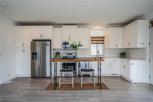 a kitchen with stainless steel appliances a refrigerator a stove a sink dishwasher and white cabinets with wooden floor