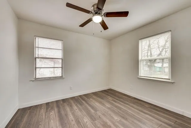 an empty room with wooden floor ceiling fan and windows