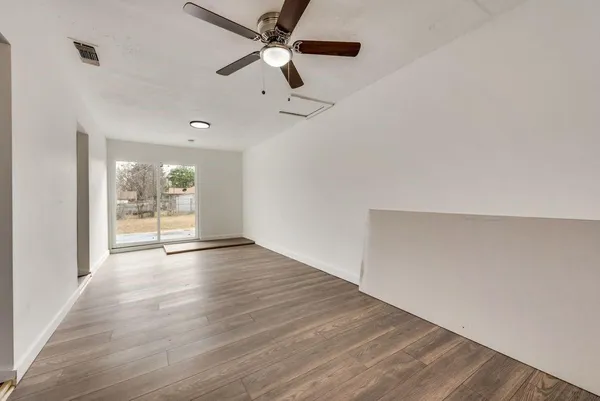 an empty room with wooden floor fan and windows