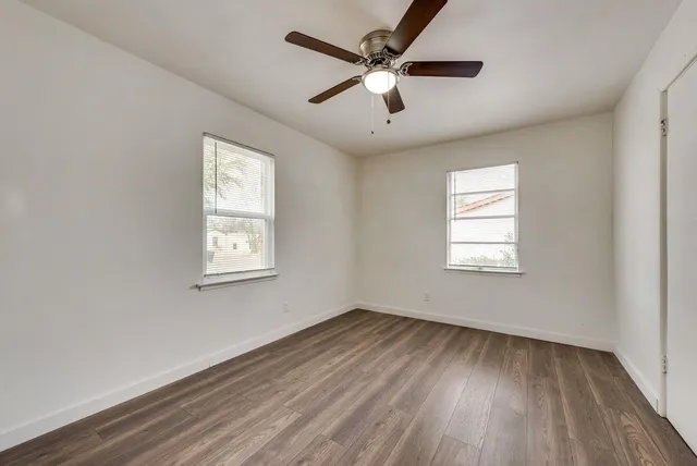 an empty room with wooden floor ceiling fan and windows