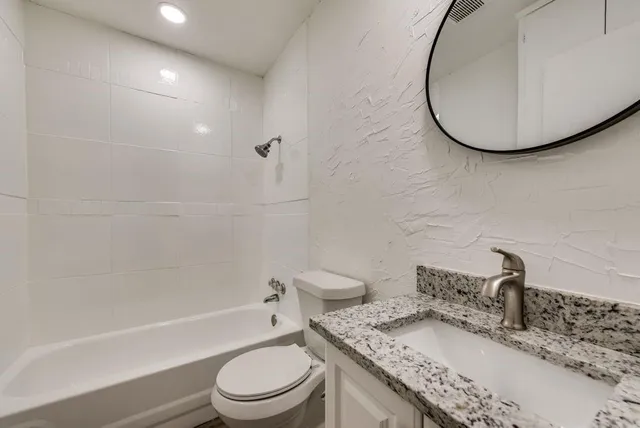 a bathroom with a granite countertop sink toilet a mirror and bathtub