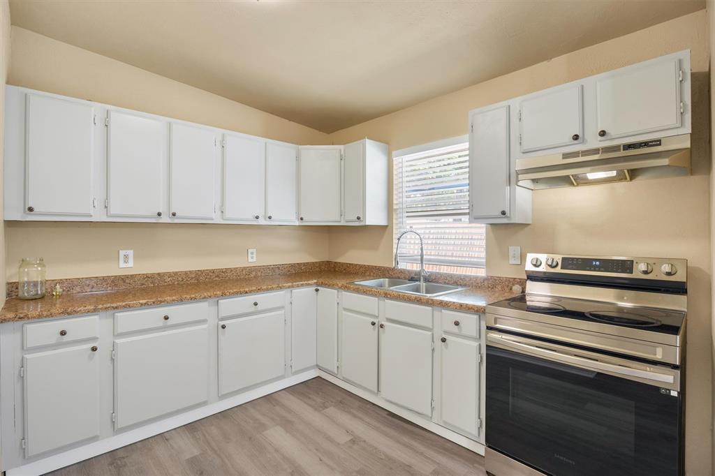 567 Tubbs Road Rockwall, TX 75032 - Photo 10 of 17 Bright, open kitchen featuring white cabinetry with ample storage, warm wood-finish flooring, granite-style countertops, stainless steel double-wall oven, and a corner sink with window overlooking the exterior
