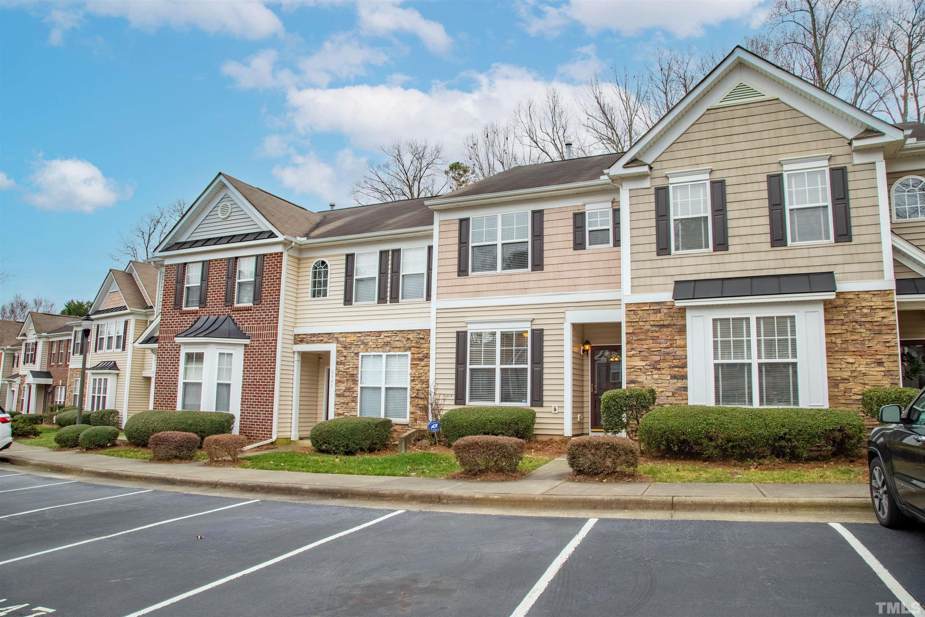 a view of a brick house with a yard plants and large tree