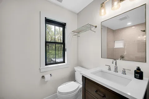 a bathroom with a toilet a sink a mirror a window and vanity