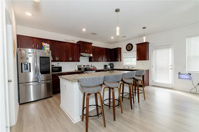 a kitchen with stainless steel appliances granite countertop a refrigerator a stove a sink a dining table and chairs with wooden floor