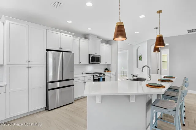 a kitchen with stainless steel appliances granite countertop a refrigerator a sink dishwasher a stove white cabinets and chairs with wooden floor