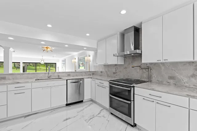 a kitchen with stainless steel appliances kitchen island granite countertop a refrigerator a stove a sink dishwasher and white cabinets with wooden floor