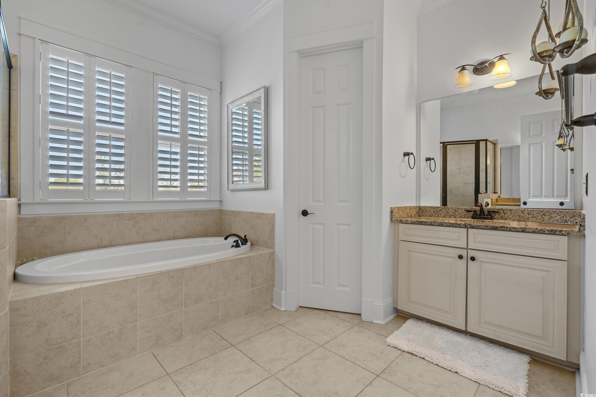 927 Iris Street Myrtle Beach, SC 29577 - Photo 22 of 40 Bathroom with vanity, a shower stall, a garden tub, light tile patterned floors, and crown molding