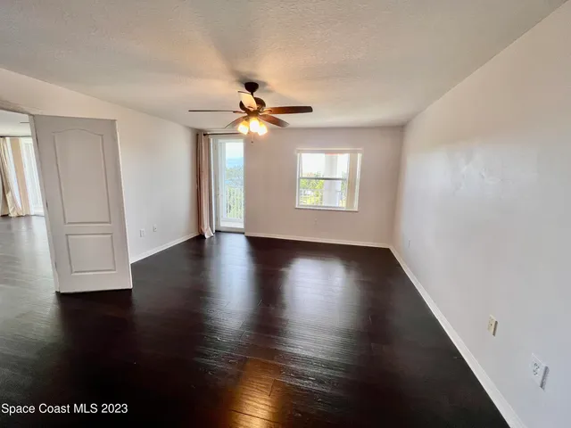 an empty room with wooden floor chandelier fan and windows