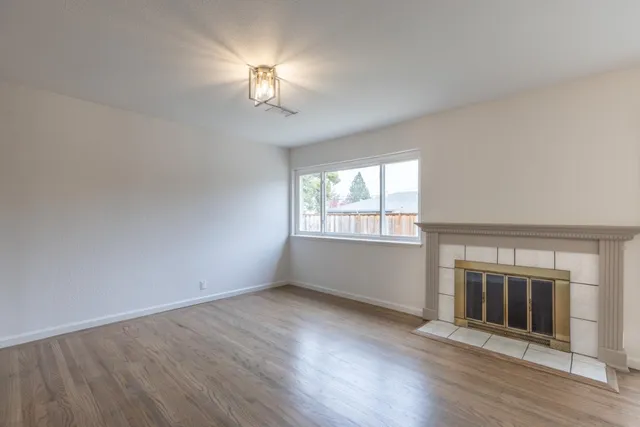 an empty room with wooden floor chandelier and fireplace