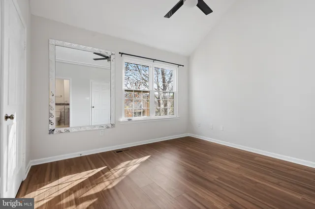 a view of an empty room with chandelier fan and wooden floor