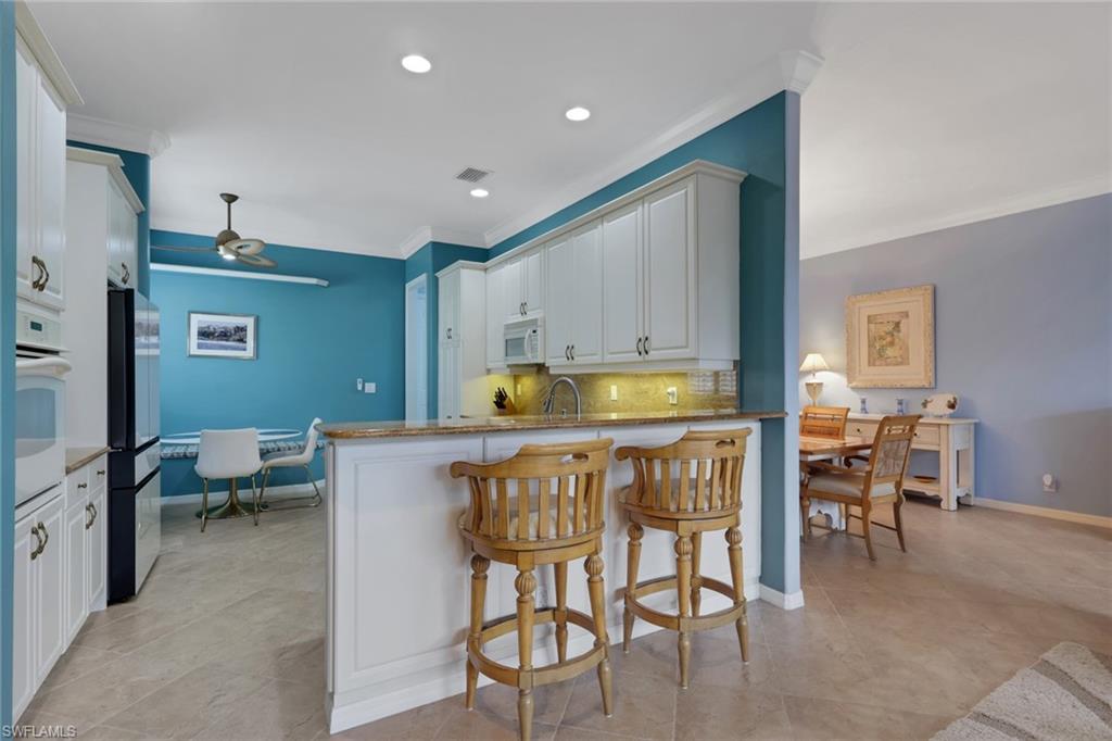 9348 Sun River Way Estero, FL 33928 - Photo 23 of 50 Kitchen featuring a kitchen bar, white cabinetry, light stone counters, a ceiling fan, and backsplash