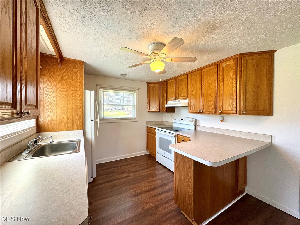 8961 Herbert Road Canfield, OH 44406 - Photo 8 of 26 Kitchen with brown cabinets, under cabinet range hood, white appliances, a peninsula, and a textured ceiling