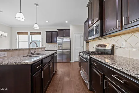 a view of kitchen with stainless steel appliances granite countertop a stove top oven a sink dishwasher a refrigerator and a dining table with wooden floor