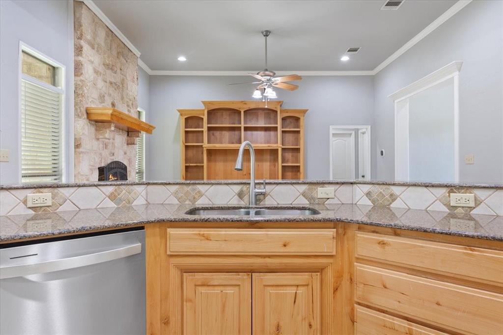 140 Oak Ridge Loop Whitney, TX 76692 - Photo 14 of 40 The kitchen features granite countertops, a stainless steel sink with a faucet, wooden cabinetry, and a tiled backsplash