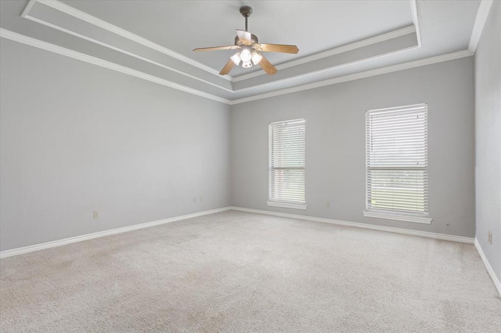 140 Oak Ridge Loop Whitney, TX 76692 - Photo 20 of 40 Spacious room featuring tray ceilings with crown molding, two windows with blinds, a ceiling fan, and carpeted floors