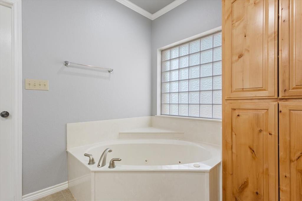 140 Oak Ridge Loop Whitney, TX 76692 - Photo 23 of 40 The bathroom features a corner soaking tub with deck-mounted fixtures, a privacy window with glass blocks, and built-in wood cabinetry