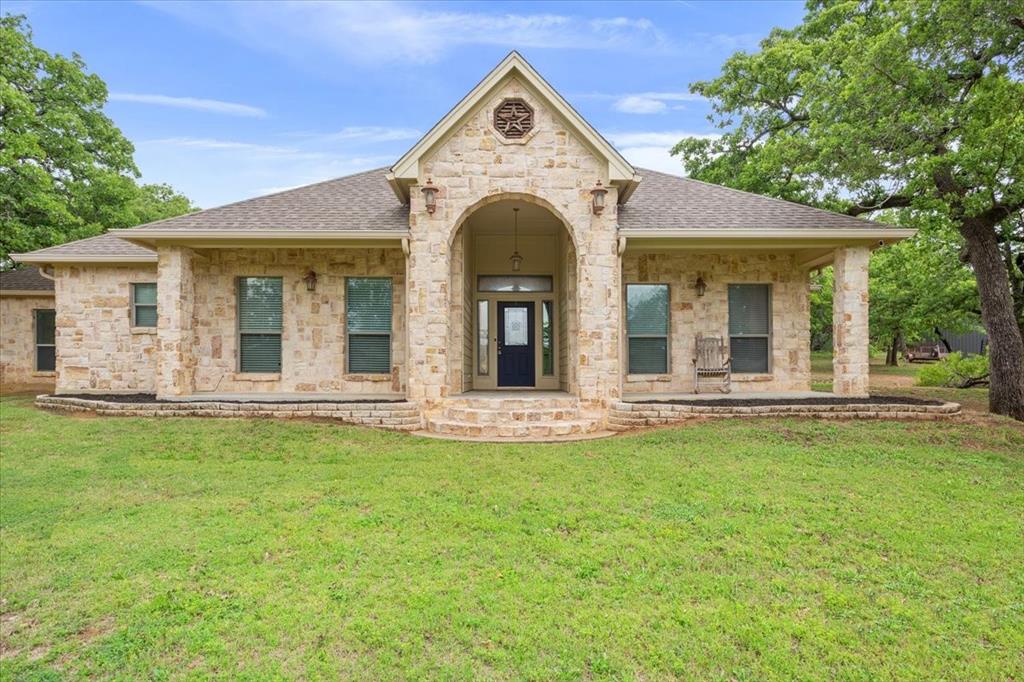 140 Oak Ridge Loop Whitney, TX 76692 - Photo 3 of 40 The property features a stone facade, a covered entry porch, a covered side porch, and a well-maintained lawn