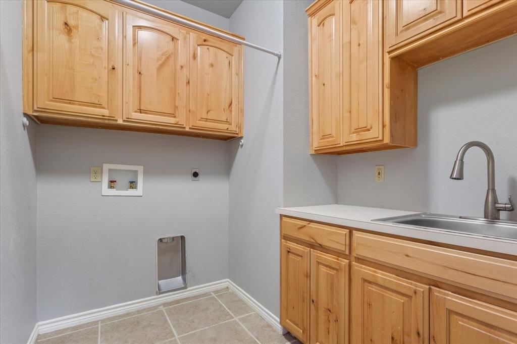 140 Oak Ridge Loop Whitney, TX 76692 - Photo 32 of 40 The utility room features natural wood cabinetry, a utility sink with a gooseneck faucet, and tiled flooring