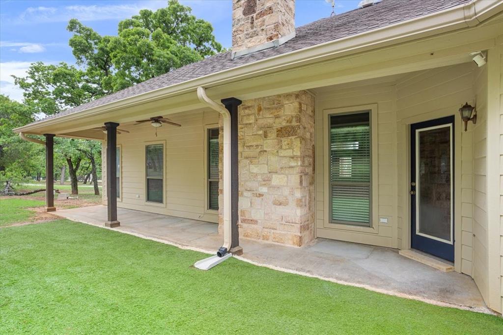 140 Oak Ridge Loop Whitney, TX 76692 - Photo 33 of 40 The property features a covered patio with pillars and a ceiling fan, a partial stone exterior, and an exterior door with a window