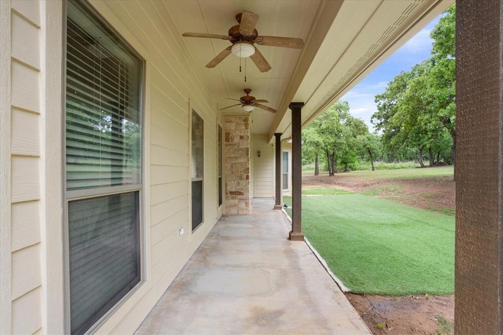 140 Oak Ridge Loop Whitney, TX 76692 - Photo 34 of 40 The property features a covered patio with ceiling fans, columns, and a stone accent pillar, overlooking a lawn area and mature trees