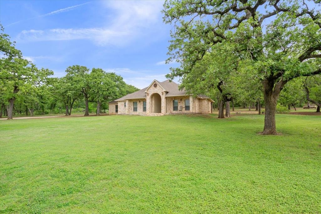 140 Oak Ridge Loop Whitney, TX 76692 - Photo 39 of 40 The property features a brick exterior with an arched entry, surrounded by a spacious lawn and mature trees