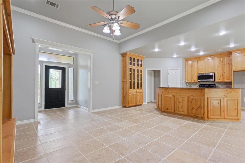 140 Oak Ridge Loop Whitney, TX 76692 - Photo 5 of 40 This open-concept interior features tile flooring throughout, a ceiling fan, and a kitchen with wooden cabinetry, a microwave, and a stovetop