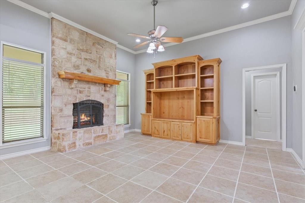 140 Oak Ridge Loop Whitney, TX 76692 - Photo 7 of 40 Living area featuring a stone fireplace with a wooden mantel, tiled flooring, built-in wooden shelving, and a ceiling fan