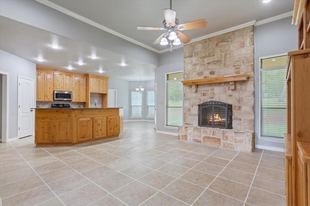 140 Oak Ridge Loop Whitney, TX 76692 - Photo 9 of 40 Spacious open-concept living area featuring a stone fireplace with a wood mantel, light-colored tile flooring, and a kitchen island with wood cabinetry and a dark countertop