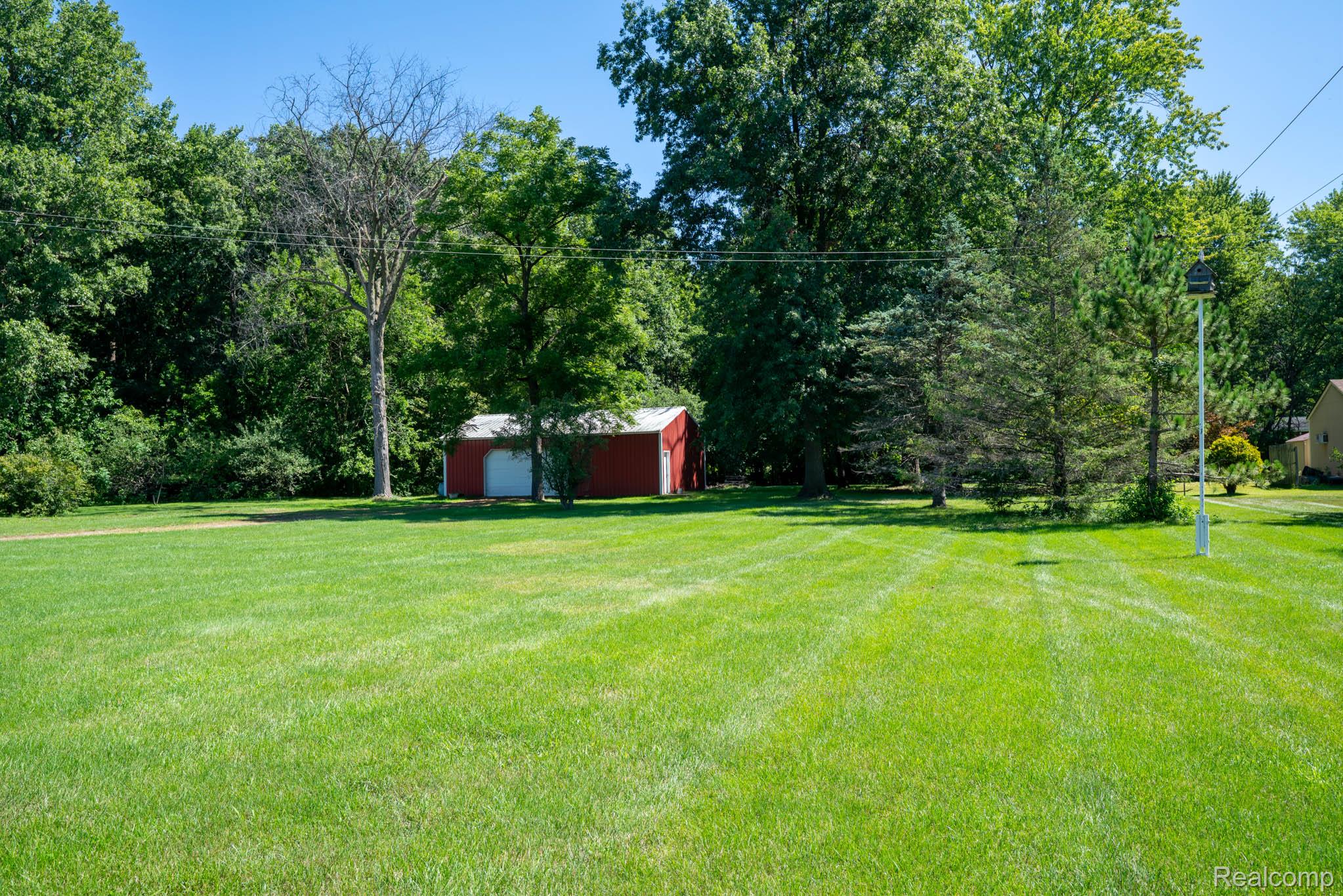 12900 Maxwell Road Carleton, MI 48117 - Photo 22 of 59 Expansive green lawn with a red storage shed and dense tree line