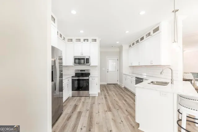 a kitchen with stainless steel appliances a stove top oven a sink a refrigerator white cabinets and wooden floor