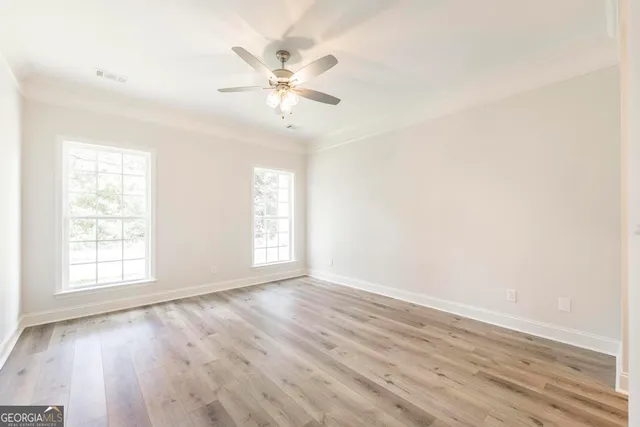 an empty room with wooden floor chandelier fan and windows