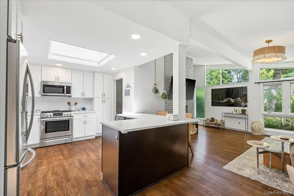 a open kitchen with stainless steel appliances a stove top oven a sink dishwasher a refrigerator white cabinets and wooden floor next to a window