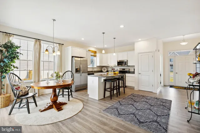 a kitchen with stainless steel appliances kitchen island granite countertop a stove a refrigerator a sink a dining table and chairs with wooden floor