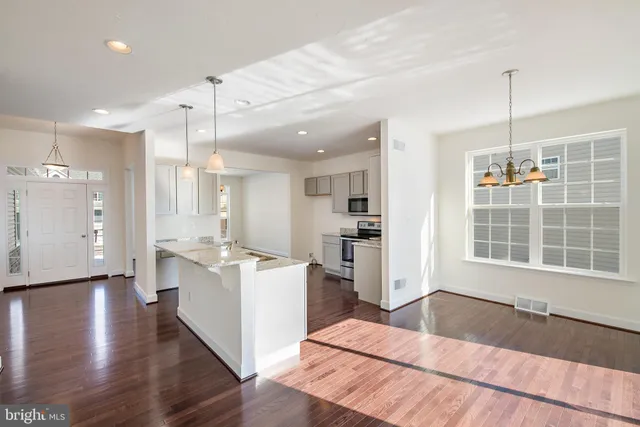 a open kitchen with stainless steel appliances kitchen island granite countertop a refrigerator a stove a sink and white cabinets with wooden floor