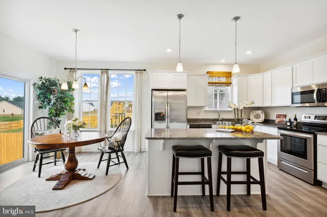 a kitchen with stainless steel appliances granite countertop a stove a refrigerator a kitchen island a table and chairs