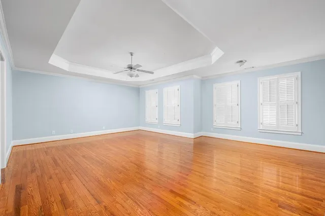 a view of an empty room with chandelier fan and wooden floor