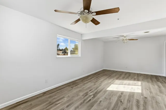 an empty room with wooden floor ceiling fan and windows