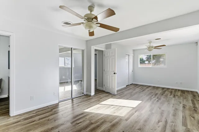 a view of an empty room with wooden floor and a ceiling fan