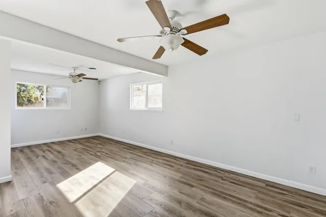 an empty room with wooden floor fan and windows