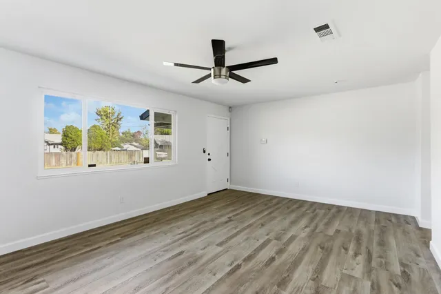 an empty room with wooden floor ceiling fan and windows