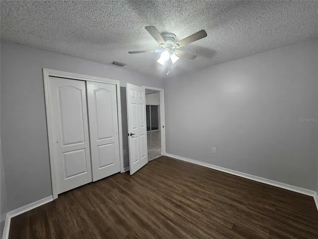 a view of an empty room with wooden floor and a fan