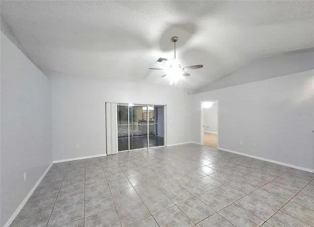 an empty room with chandelier fan and windows