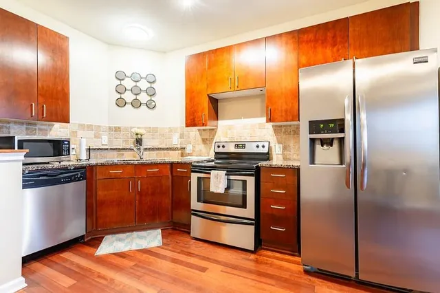 a kitchen with stainless steel appliances granite countertop a refrigerator a stove and a sink with wooden floor
