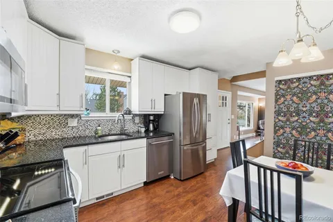 a kitchen with stainless steel appliances granite countertop a refrigerator a sink a stove and white cabinets with wooden floor