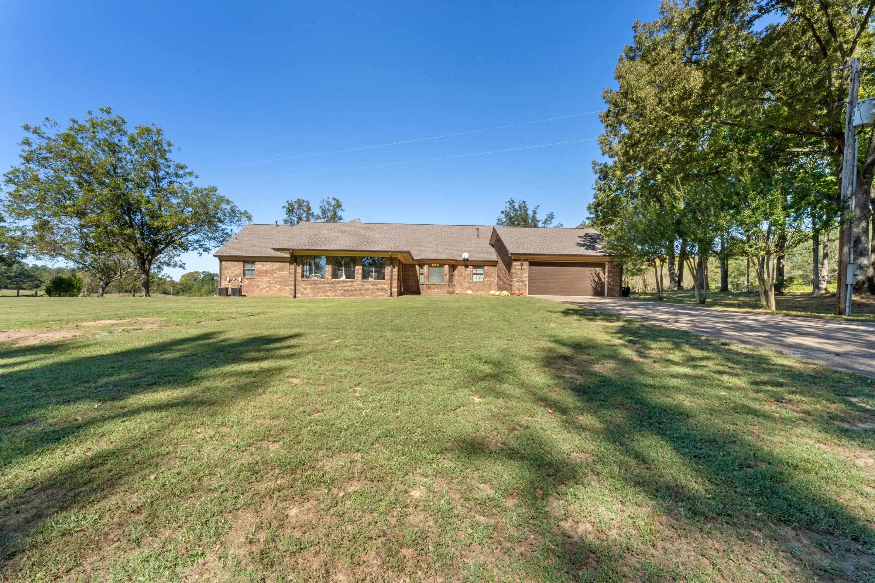 650 Blain Road Rossville, TN 38066 - Photo 29 of 32 Rear view of the home showcasing the attached garage, spacious backyard, and tranquil setting surrounded by mature trees and open acreage.