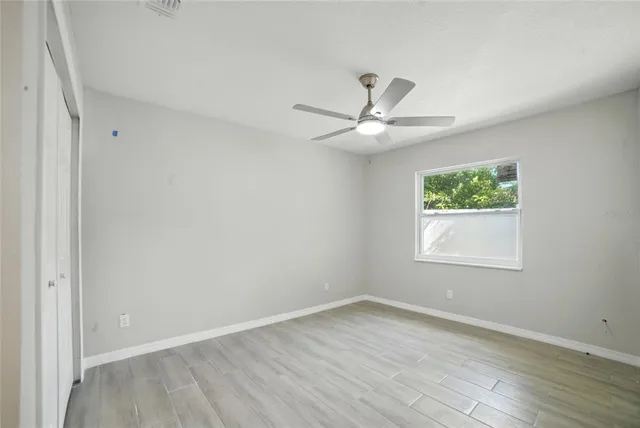 an empty room with wooden floor window and ceiling fan