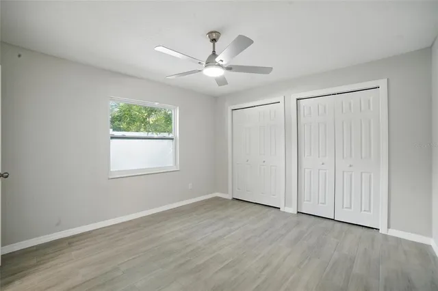 an empty room with wooden floor ceiling fan and windows